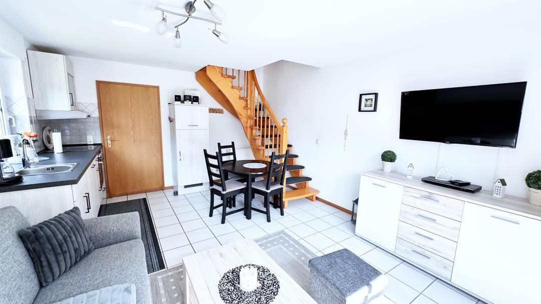 Wohnung mit Küche, Essbereich und Wohnzimmer mit Fernseher und Holztreppe.