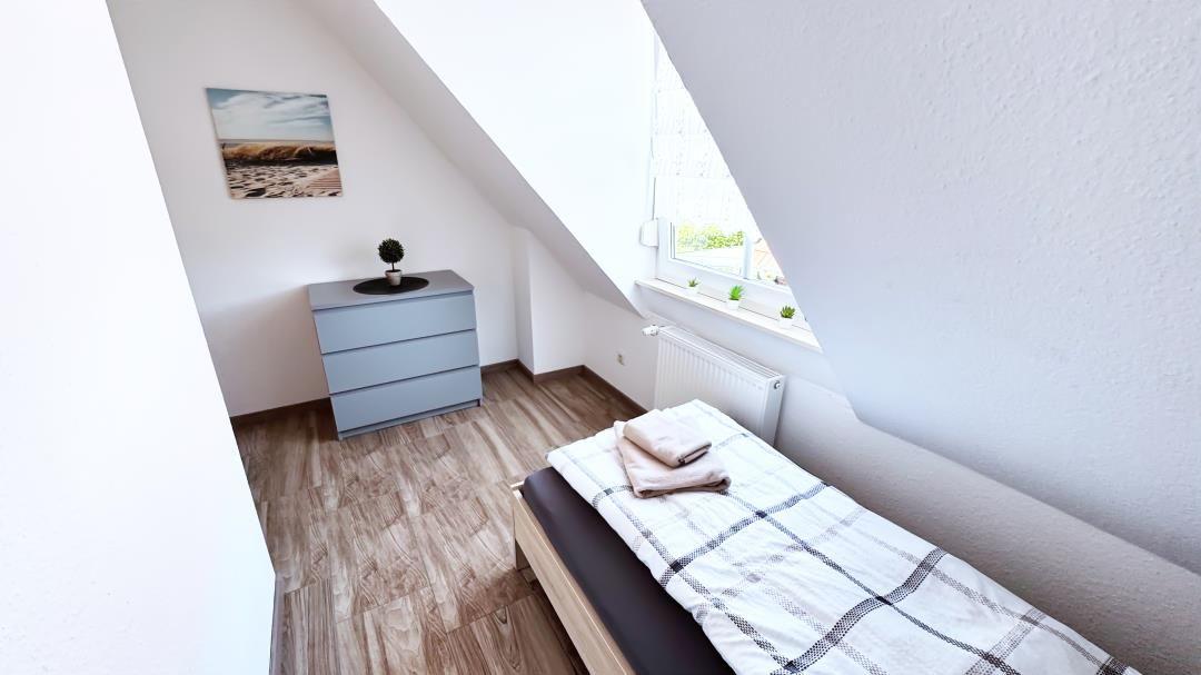 Schlafzimmer mit Dachschrägen, Bett, Kleiderschrank und Fenster.