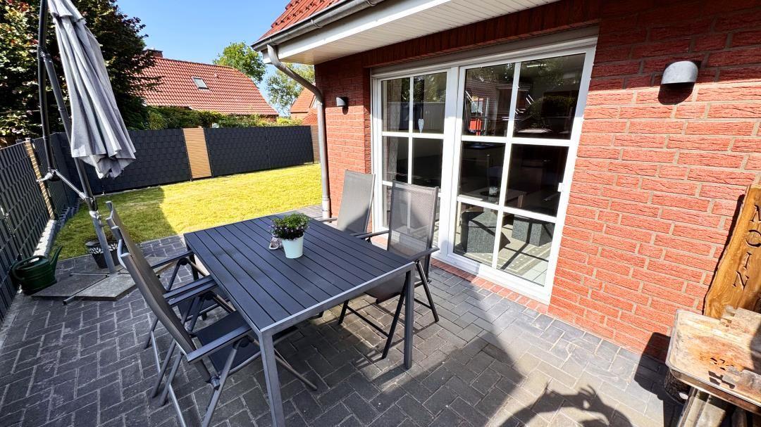 Terrasse mit Tisch, Stühlen und Sonnenschutz. Hintergrund: Garten und Hauswand.