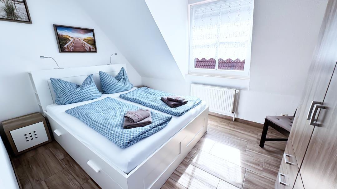 Schlafzimmer mit Doppelbett, Fenster und Kleiderschrank.