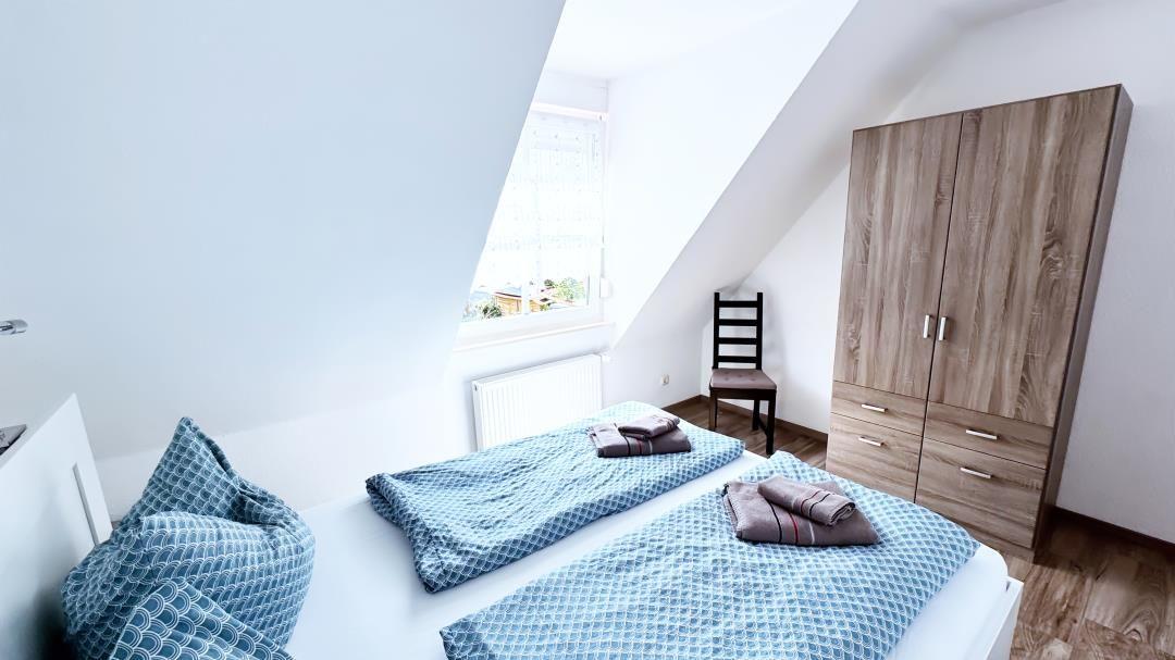 Schlafzimmer mit Dachschrägen, Bett, Kleiderschrank und Fenster.