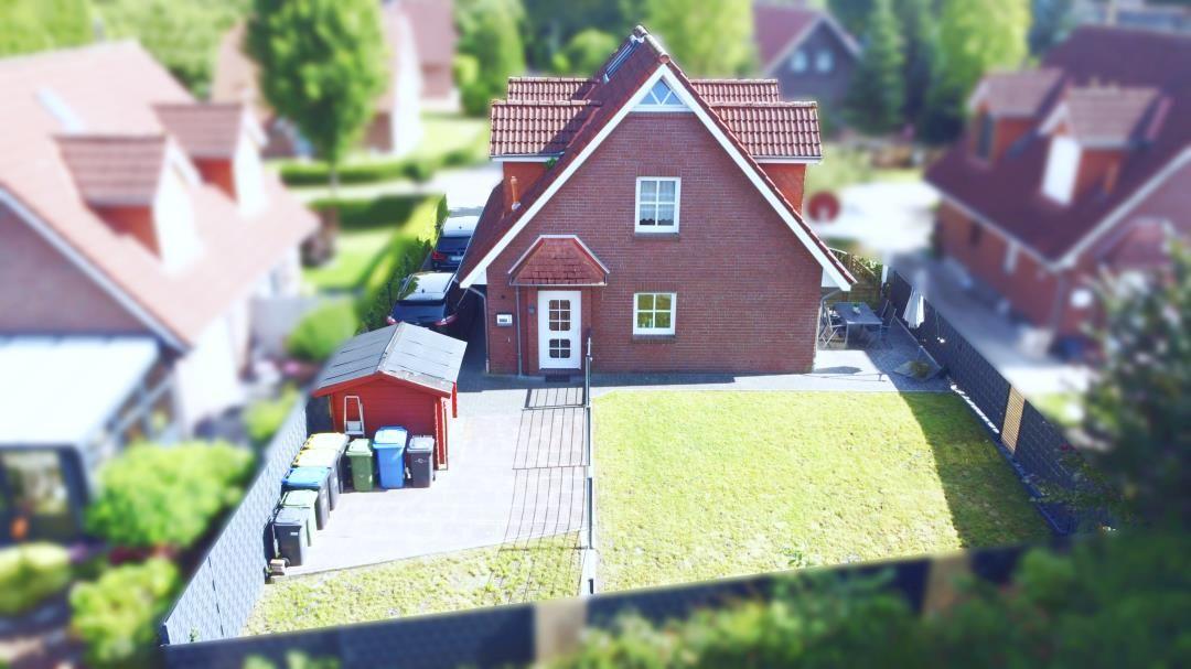 Rotes Backsteingebäude mit Vorgarten und Garage. Gartenhaus und Müllcontainer sind sichtbar.