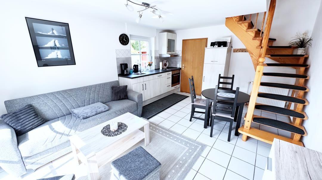 Wohnbereich mit Sofa, Esstisch und Holztreppe.