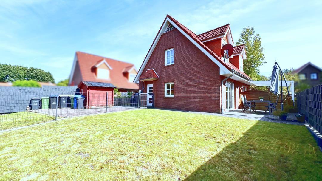 Rotes Backsteingebäude mit Garten, Terrasse und Sonnenschirm.