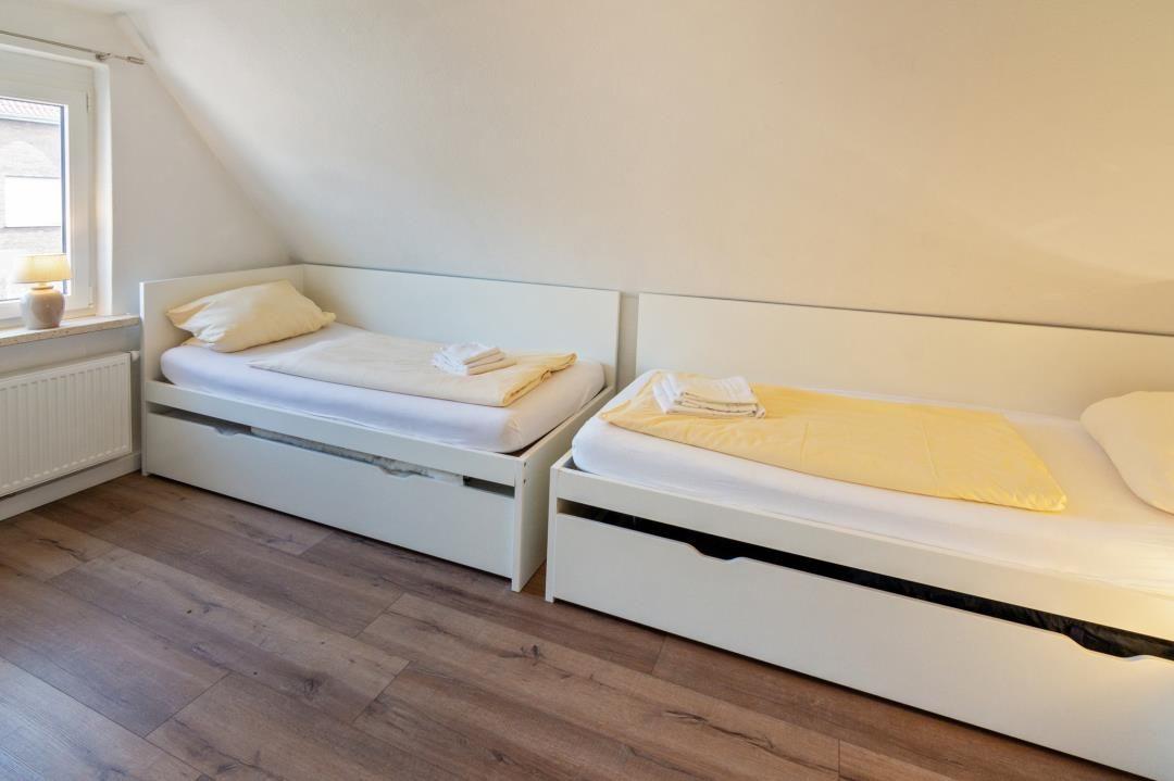 Zwei weiße Einzelbetten mit gelben Decken und Kissen stehen in einem Raum mit Holzboden und schrägem Dach.