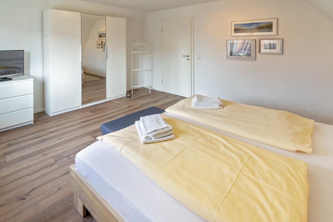 Zwei Betten mit gelben Bettdecken, weißer Schrank und Holzboden.
