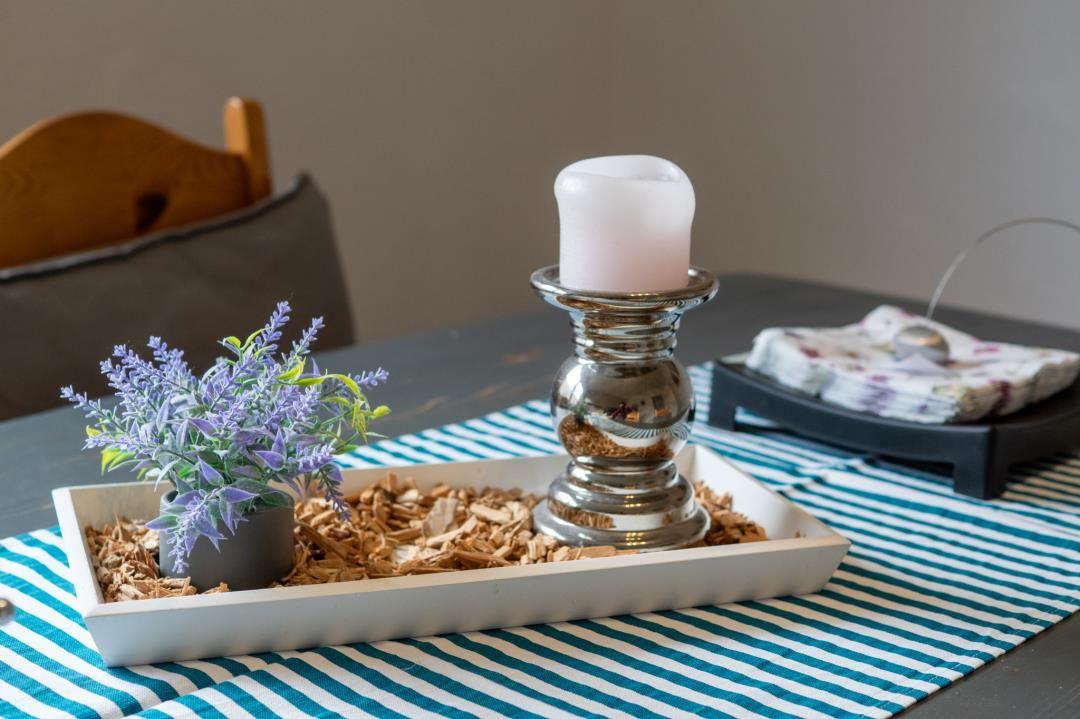 Tisch mit Kerze, Pflanze und Holzmulch auf Streifen-Tischdecke
