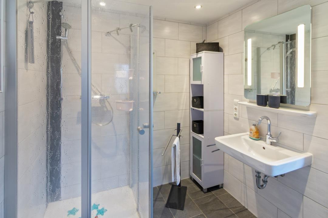 Badezimmer mit Dusche, Waschbecken und Spiegel