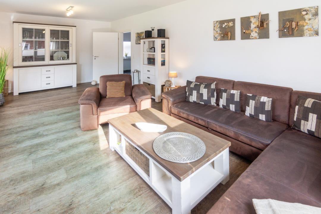Wohnzimmer mit braunem Sofa, Holzfußboden und weißen Schränken.