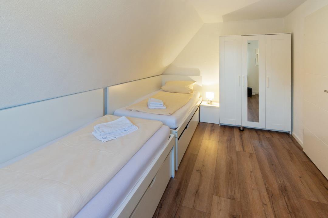 Zimmer mit zwei Einzelbetten, Holzboden und weißem Schrank