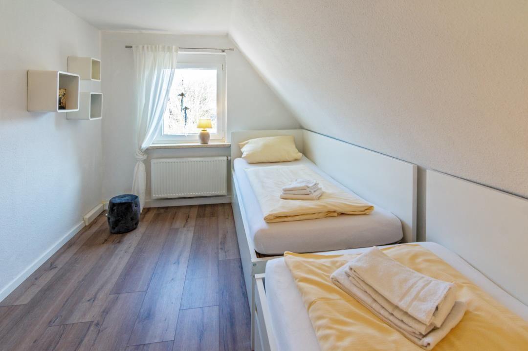 Zwei Betten mit gelben Bettwäsche, Holzboden und Fenster mit Vorhang.
