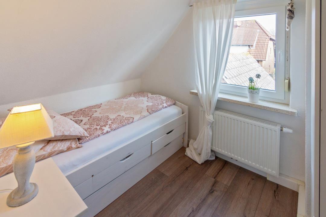 Schlafzimmer mit Dachschräge, Bett mit Schubladen, Fenster mit Vorhang und Heizkörper.