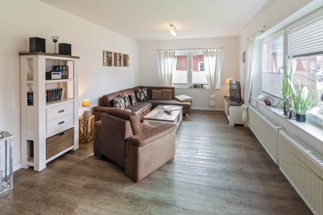 Wohnzimmer mit braunem Sofa, Holzboden und großen Fenstern.