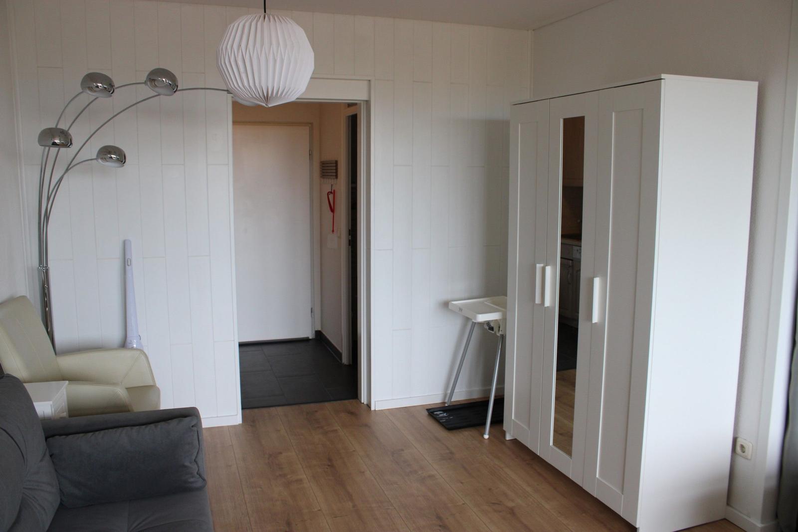 Living room with sofa, floor lamp, and wardrobe. Wooden floor and white walls.