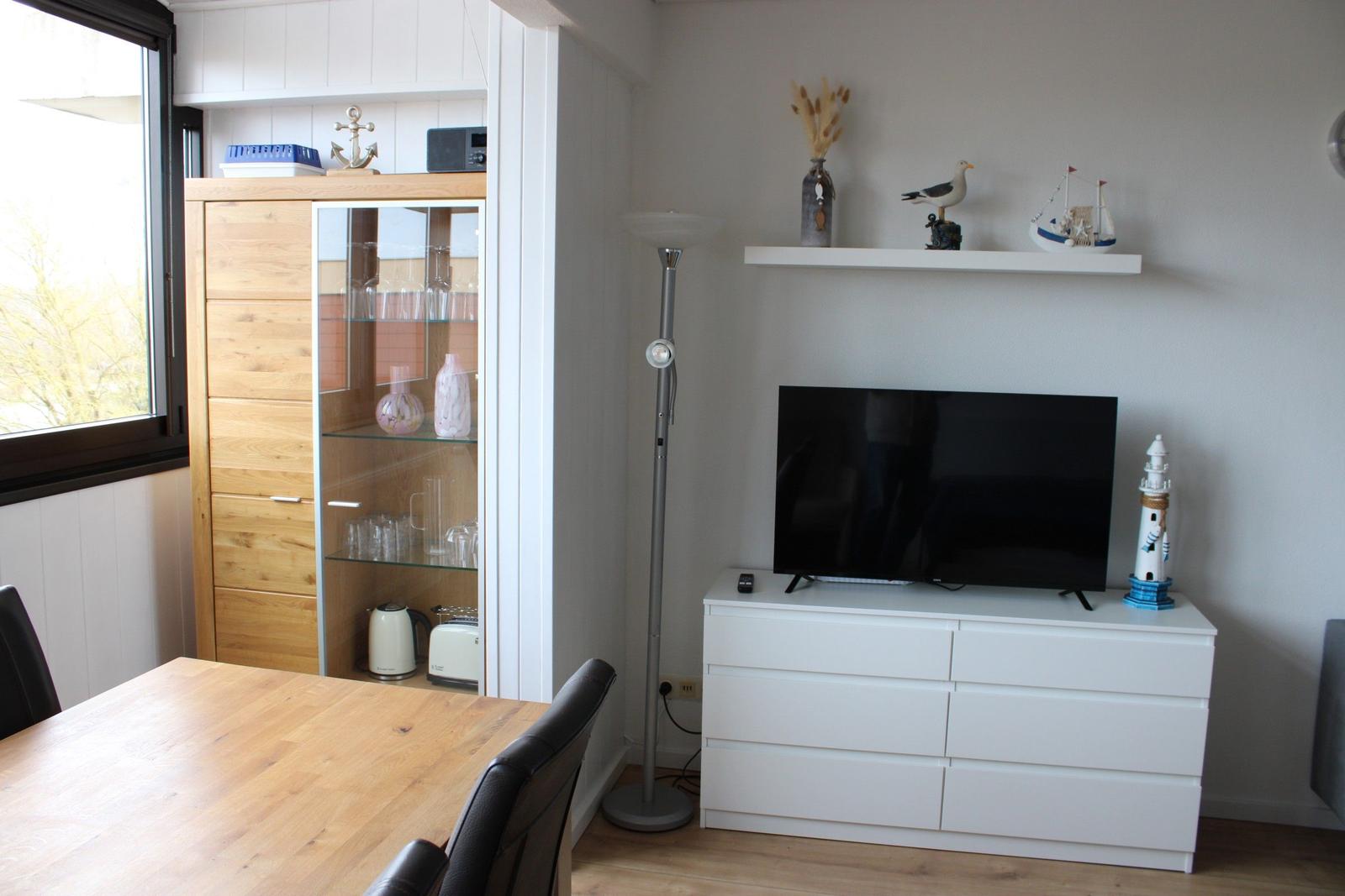 Living room with TV, cabinet, and floor lamp. Decor includes sailboat and lighthouse.