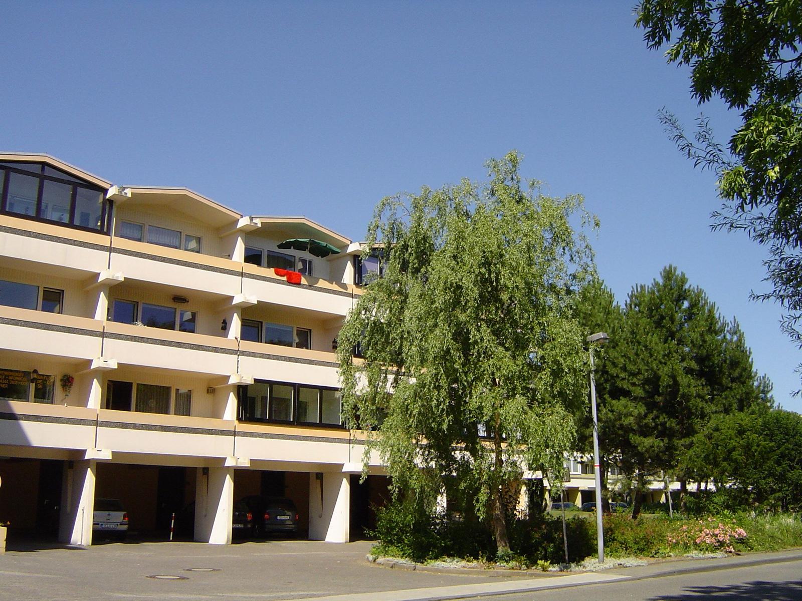 Multi-family building with balconies and parking spaces under trees.