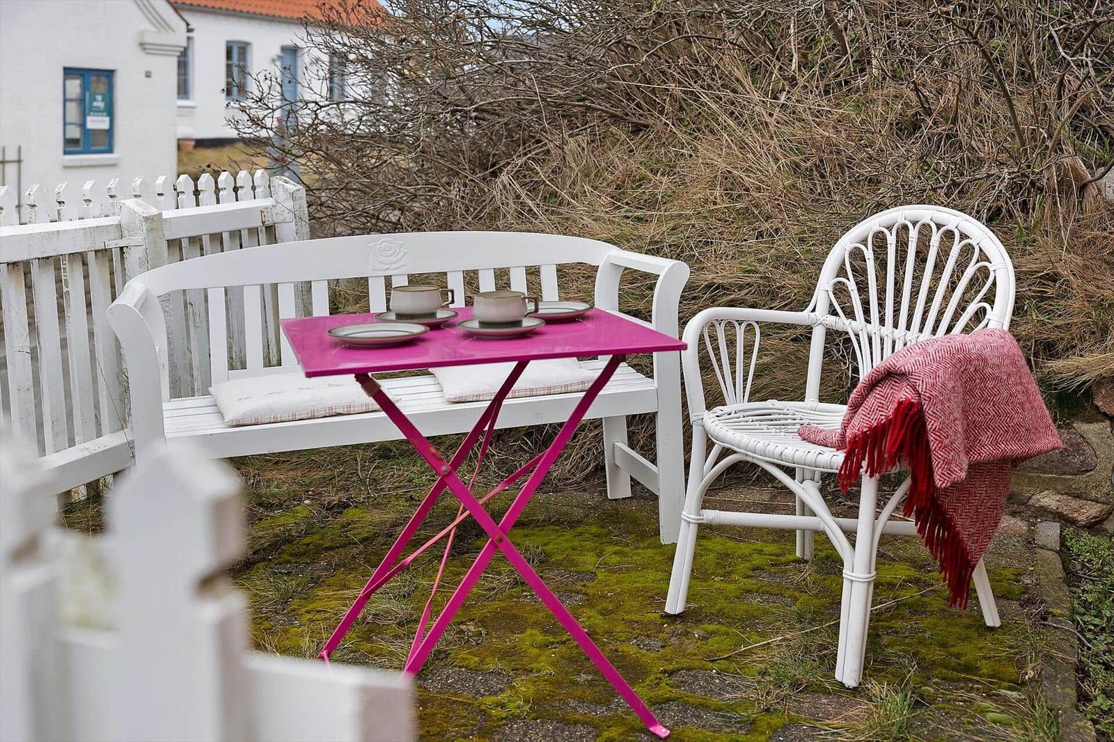 Outdoor area with white sofa, chair, and pink table. Two cups are on the table.