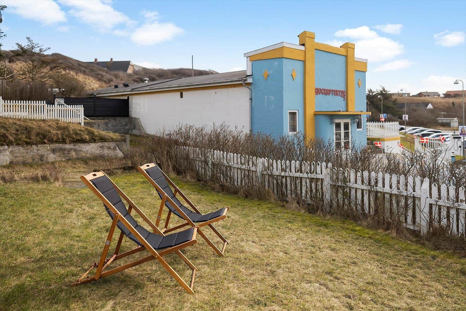Two deck chairs sit on a lawn in front of a blue house with a white fence.