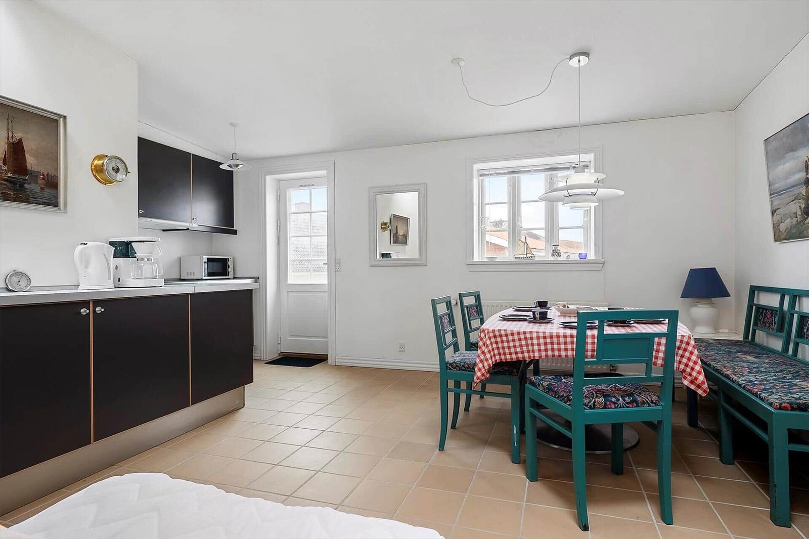 Kitchen with dining area, table with red-and-white checkered cloth and green chairs.