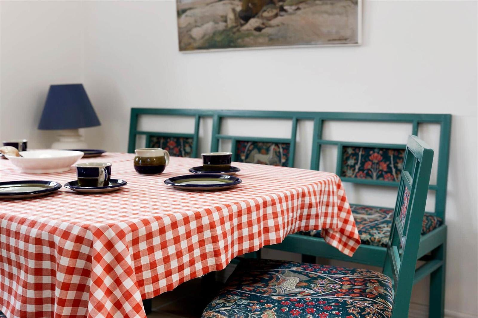 Dining table with checkered tablecloth and green chairs with floral upholstery.
