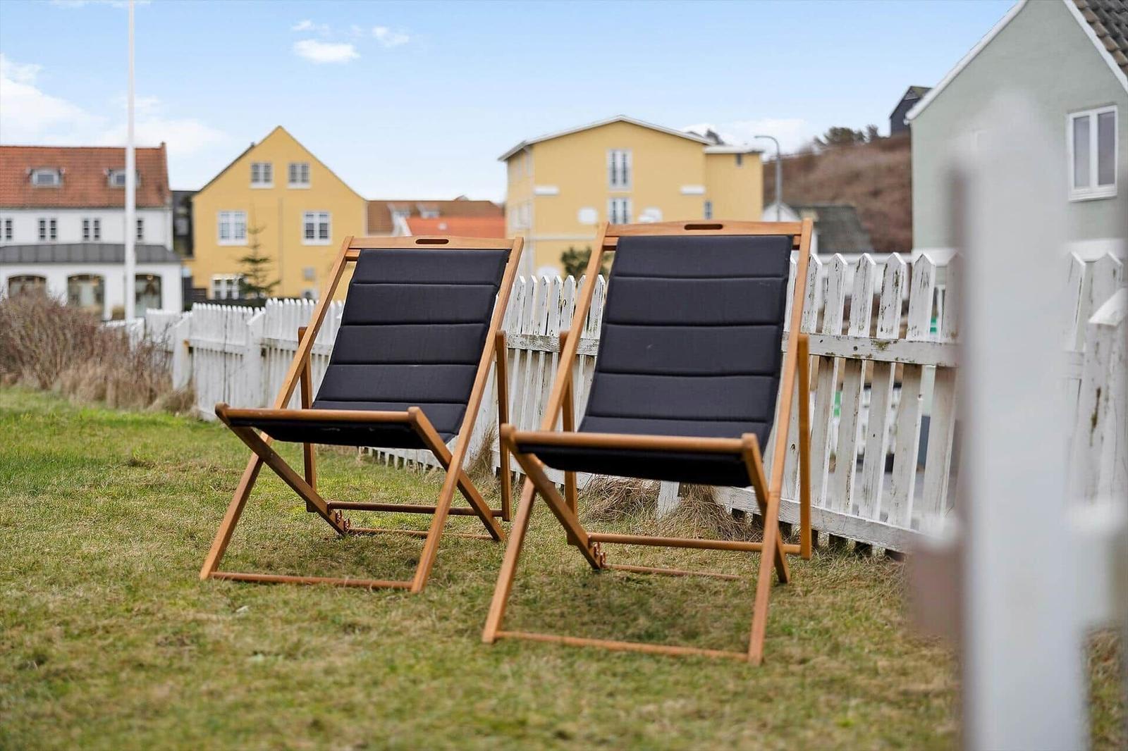 Two black lounge chairs are on a lawn behind a white fence.