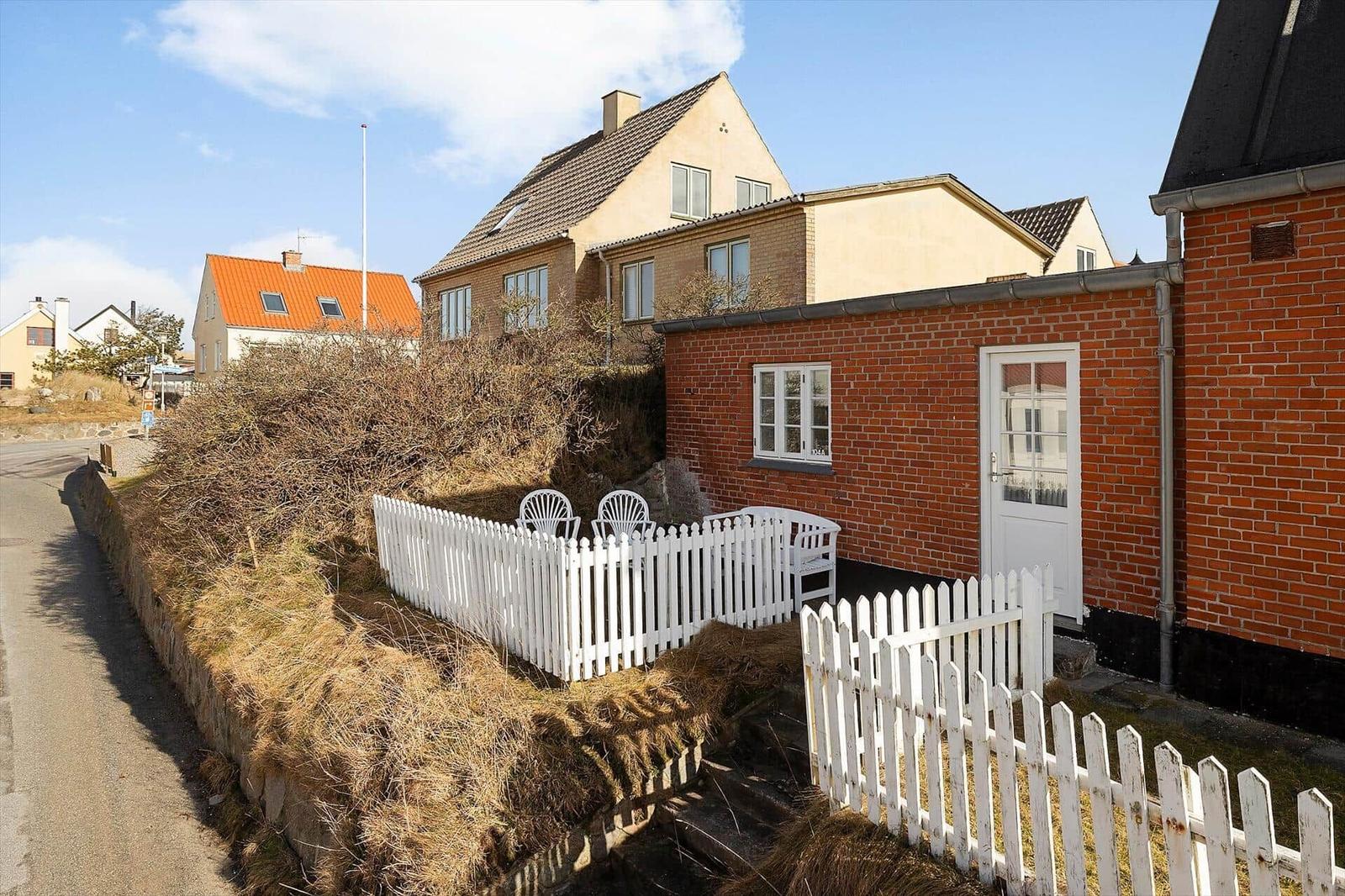 Red brick building with white door and fence. Outdoor area with chairs.