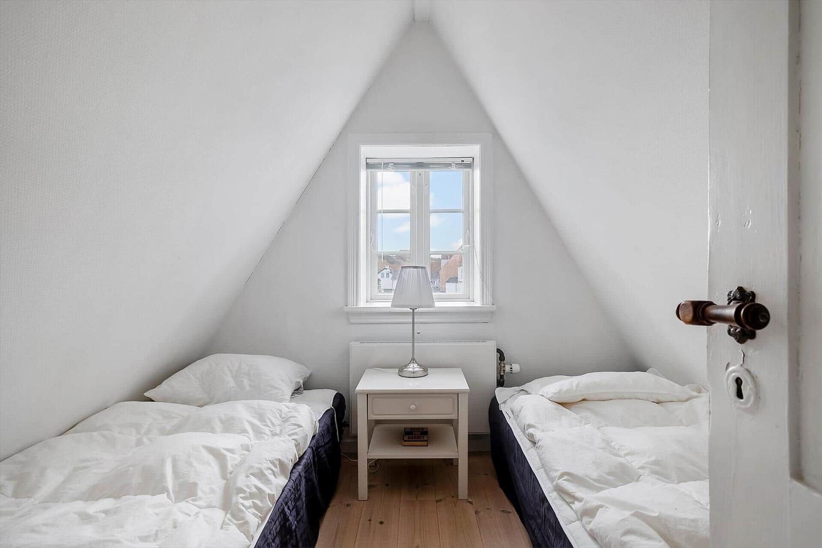 Two beds under sloped ceilings with window and nightstand.