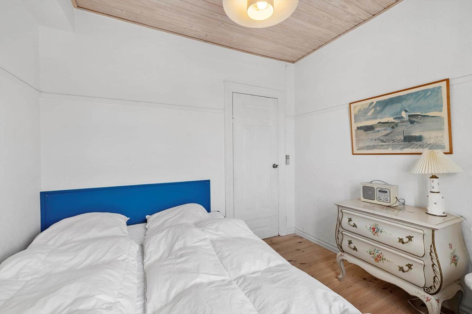 Bedroom with bed, dresser, and ceiling. Wall art and lamp on dresser.