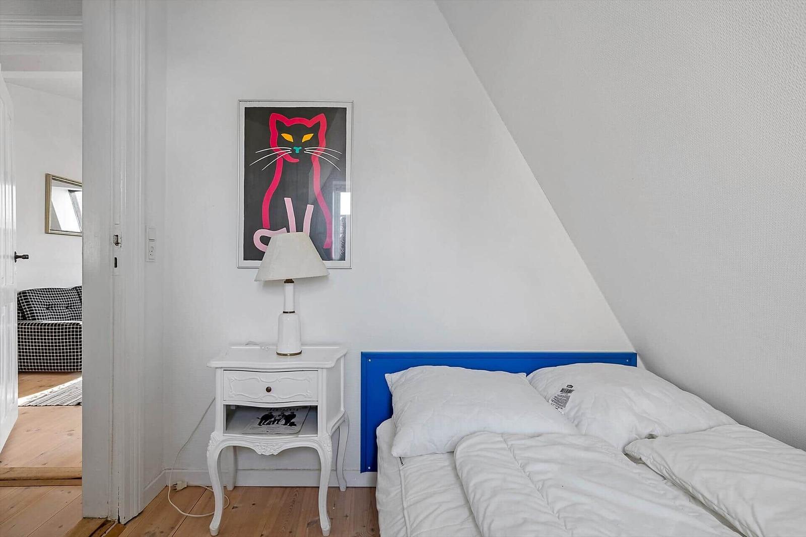 Bedroom with blue headboard, white nightstand, and cat picture on the wall.
