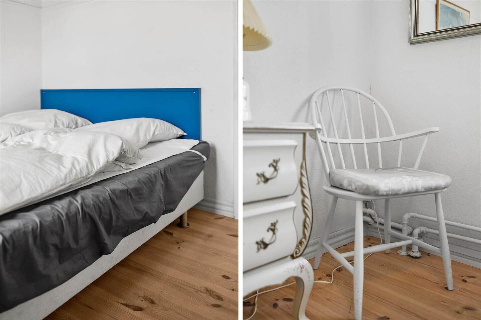 Bedroom with bed and chair. Blue headboard, white dresser, wooden floor.