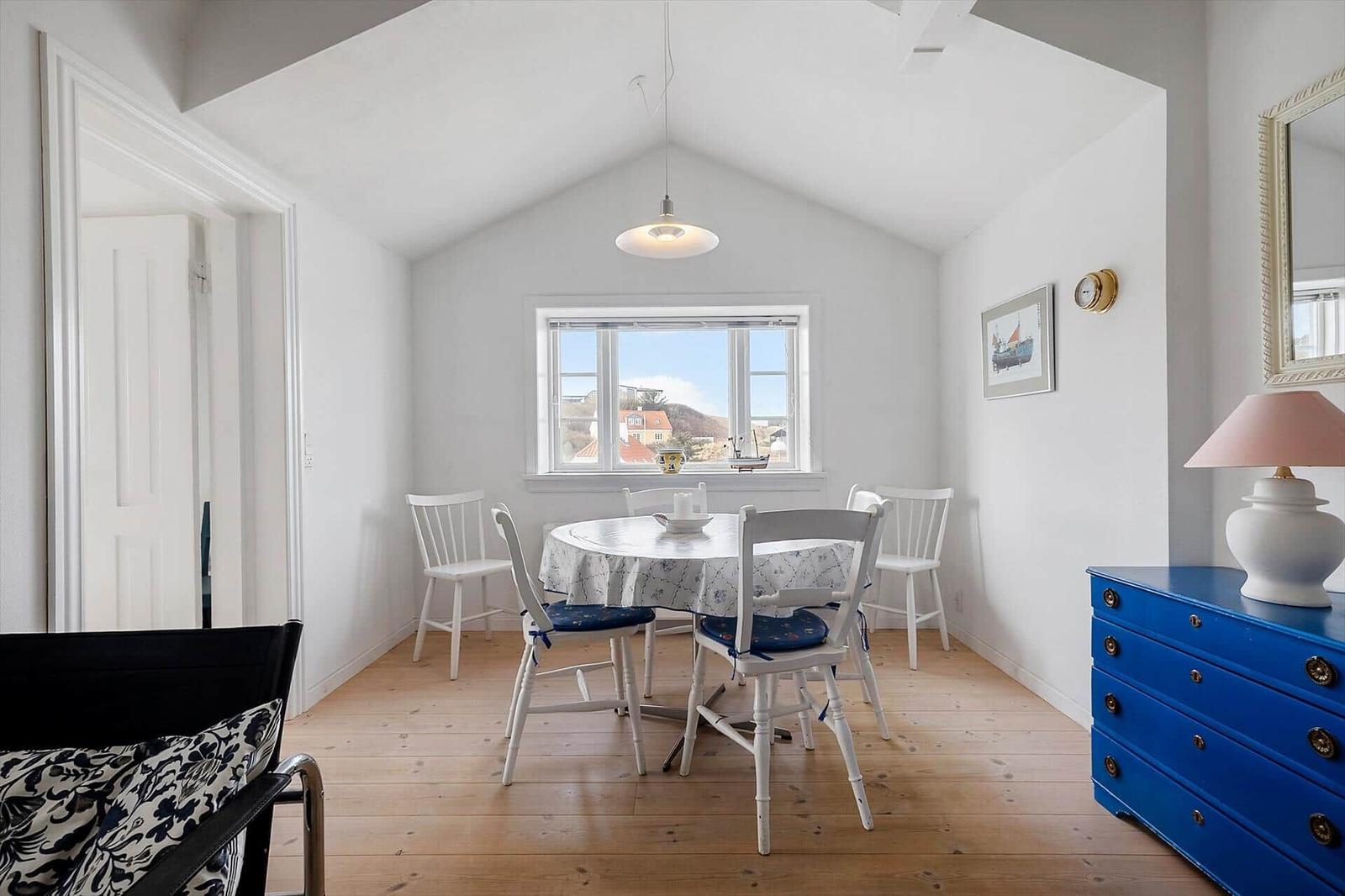 Dining room with round table, white chairs, and blue dresser. Wooden floor and window with view.