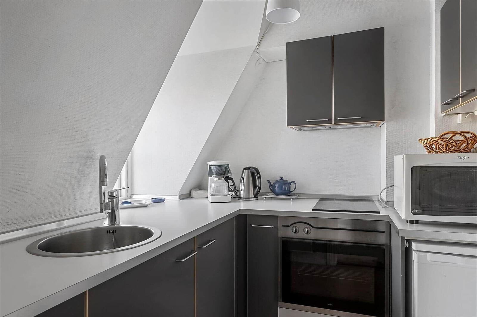 Kitchen with range hood, sink, stove, and microwave under sloped ceiling.