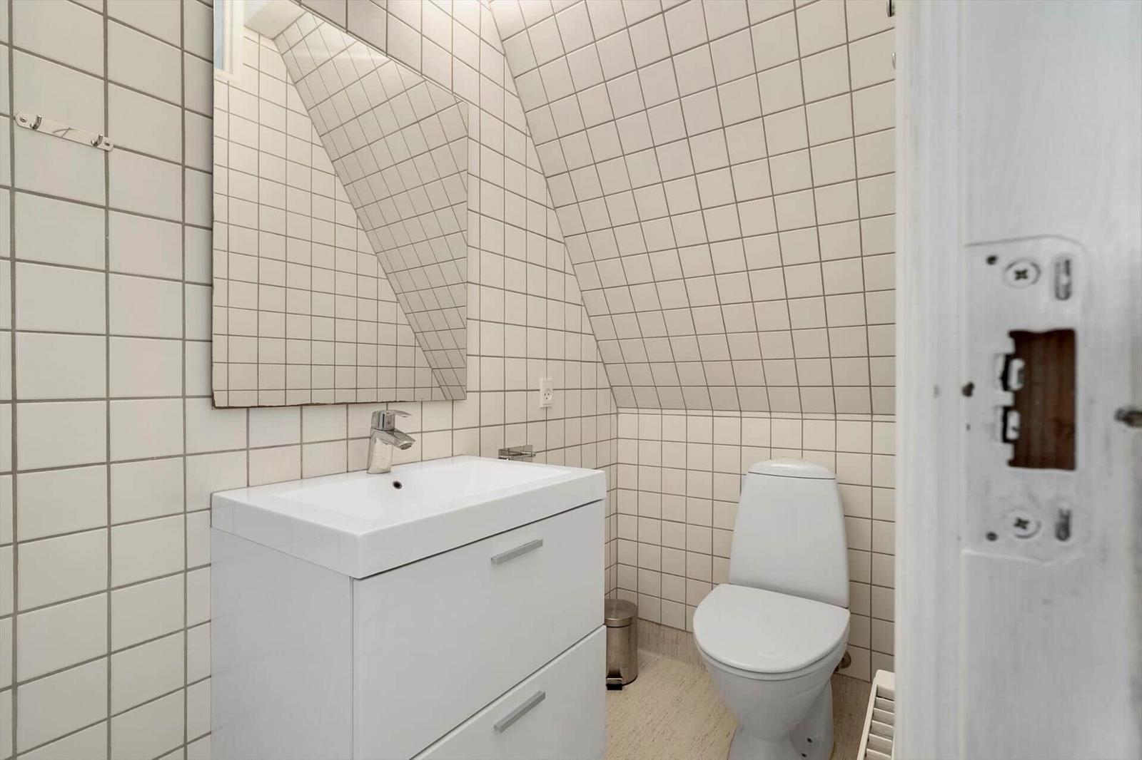 Bathroom with toilet, sink, and mirror on sloped walls.