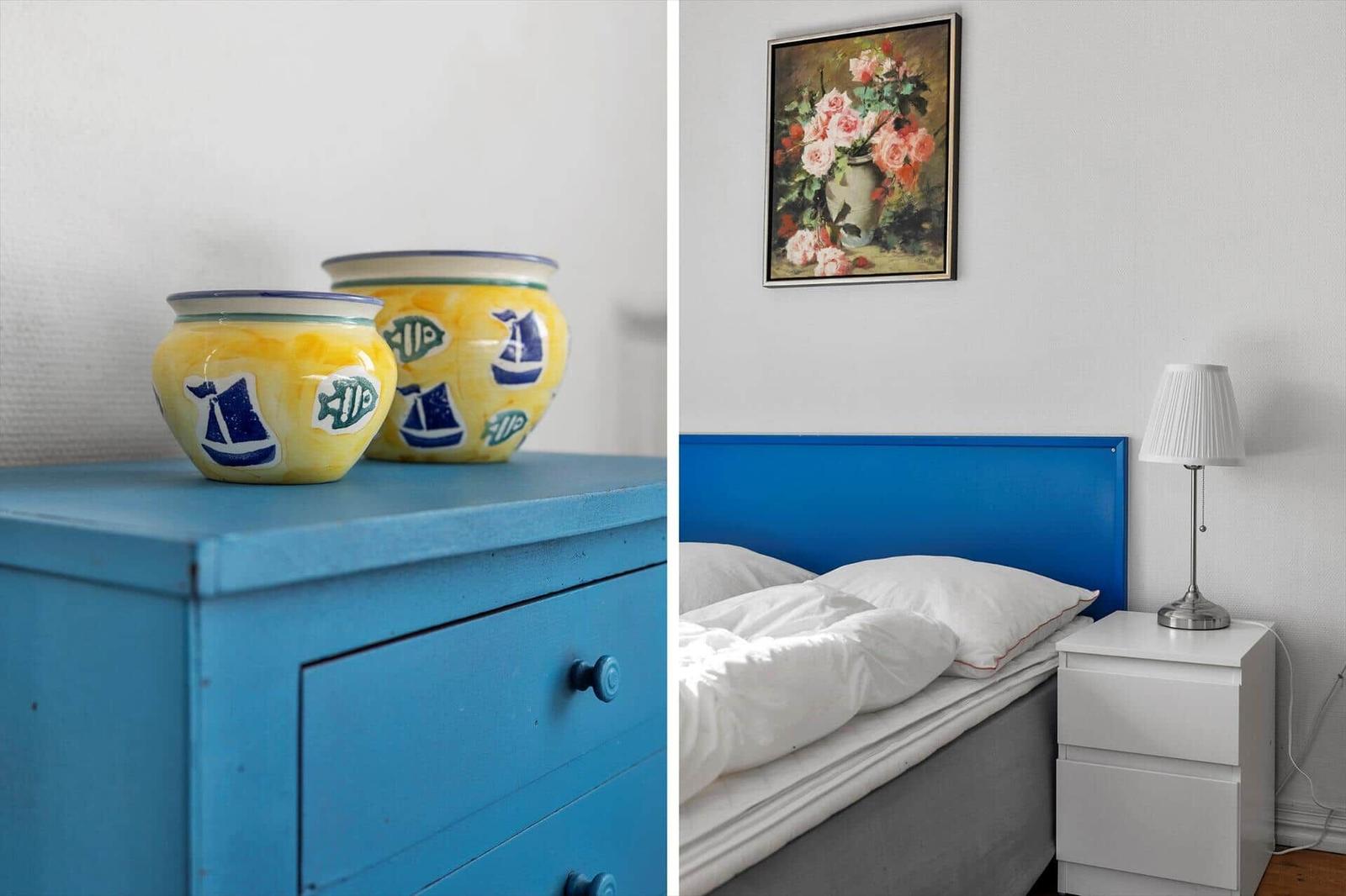 Bedroom with blue headboard, white bedside lamp, and painting on the wall.