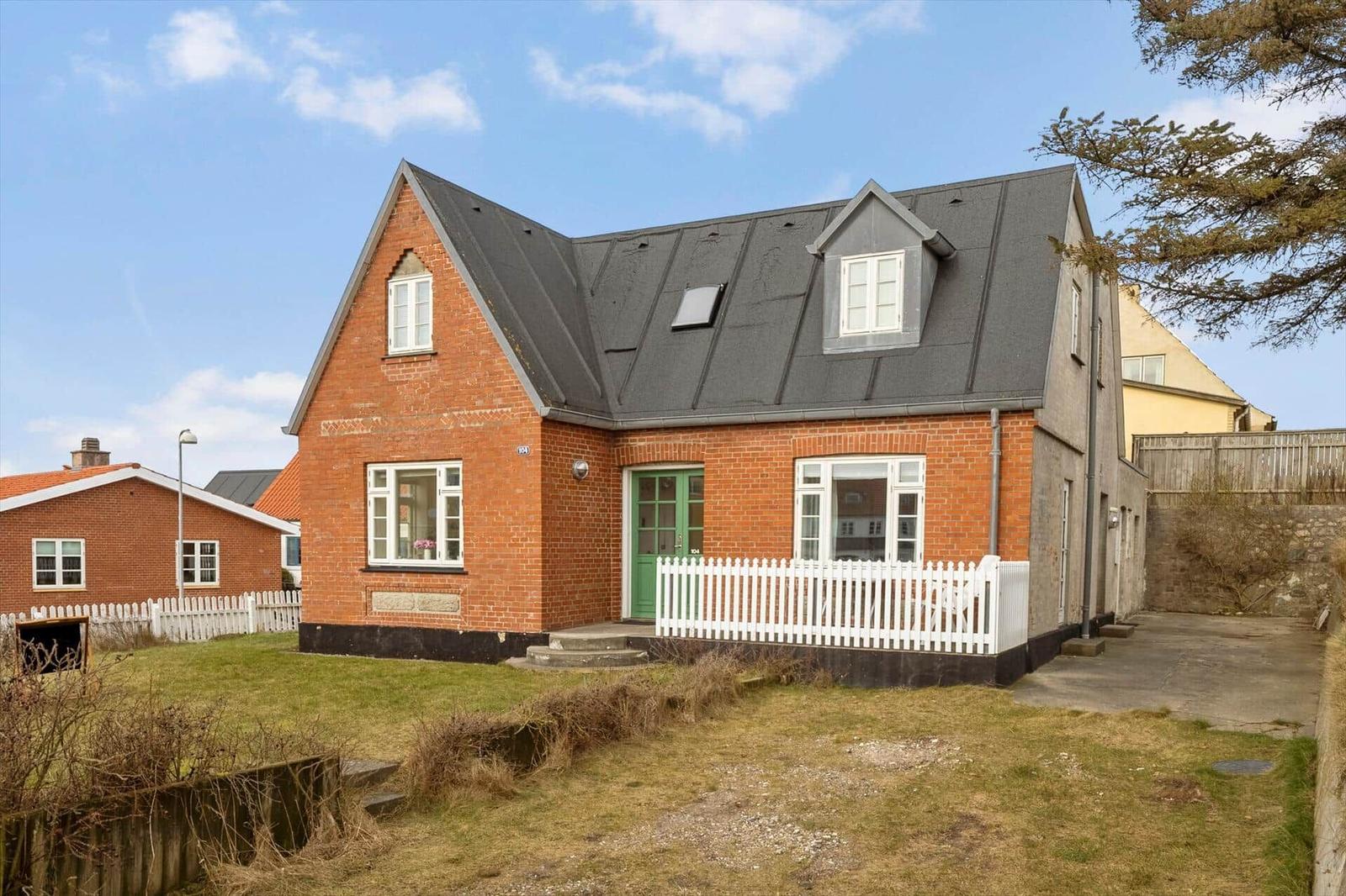 A red brick house with a green door and white fence.