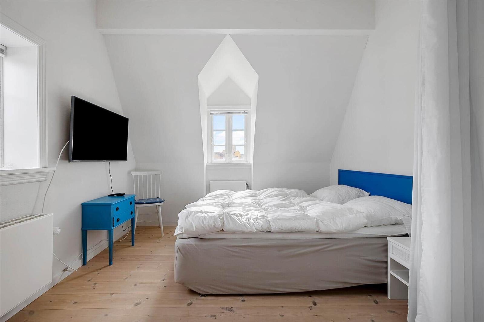 Bedroom with bed, window, and TV. Blue dresser and chair.