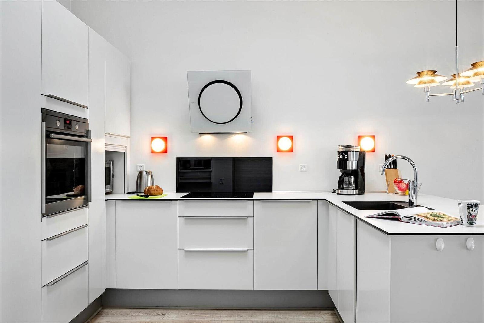 Modern kitchen with white cabinets, stainless steel appliances, and red wall lights.