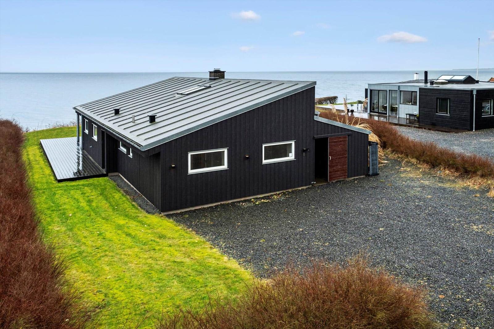 Modern villa with sea view and terrace. Black facade, green lawn, and gravel path.