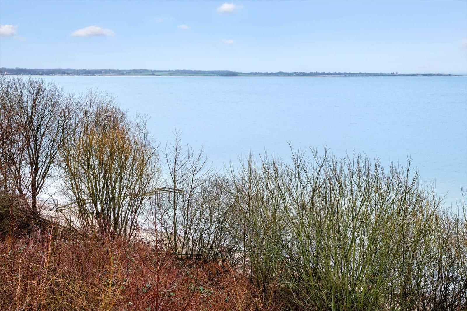 Seascape view from a cliff with trees and shrubs in the foreground.