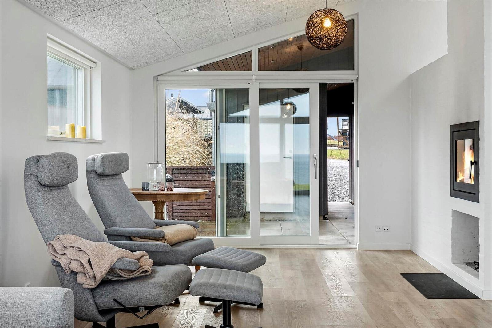 Two gray recliners with footstools stand before a glass door. A fireplace is mounted on the wall.