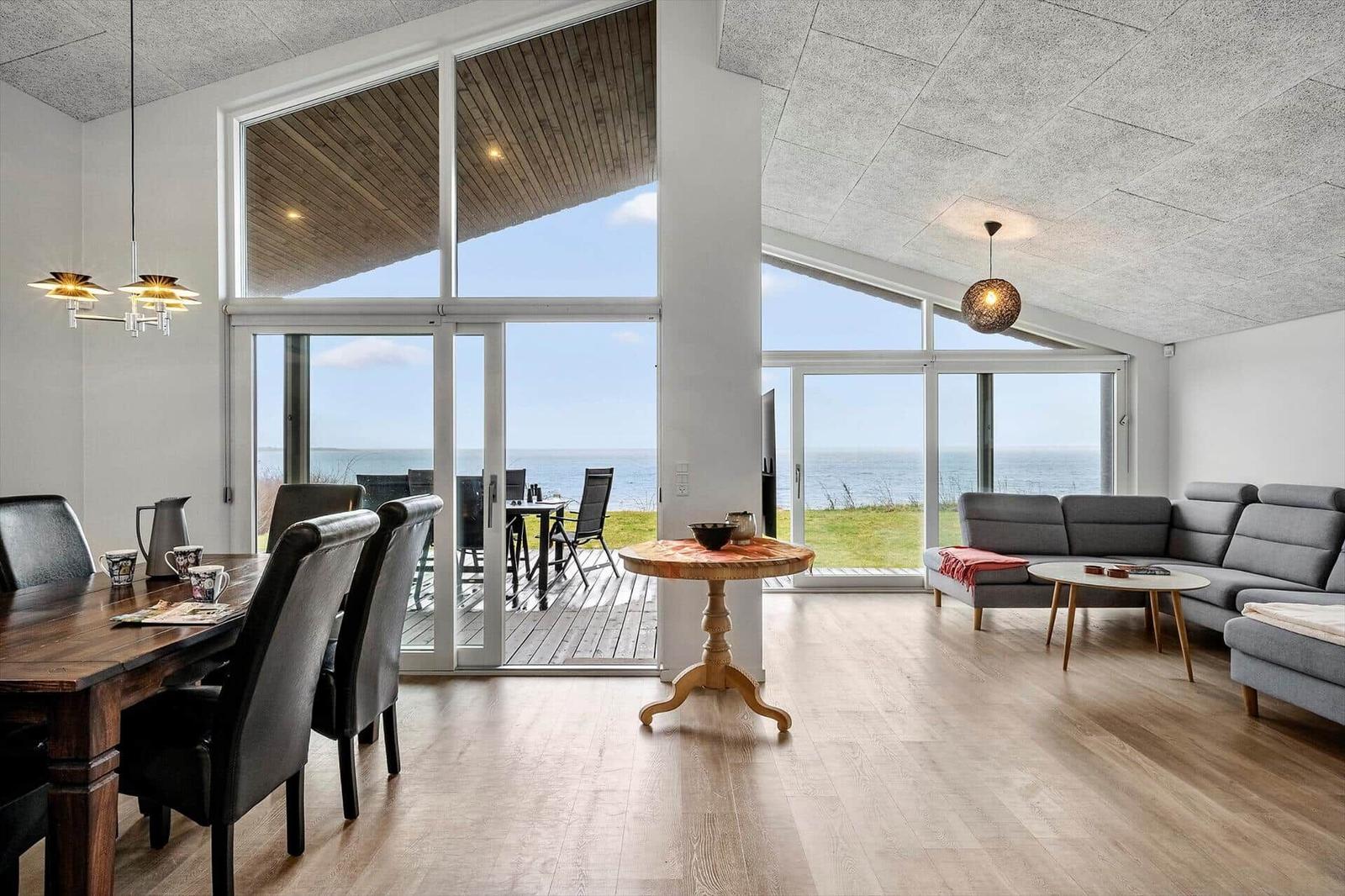 Large living and dining room with sea view through large windows and terrace.