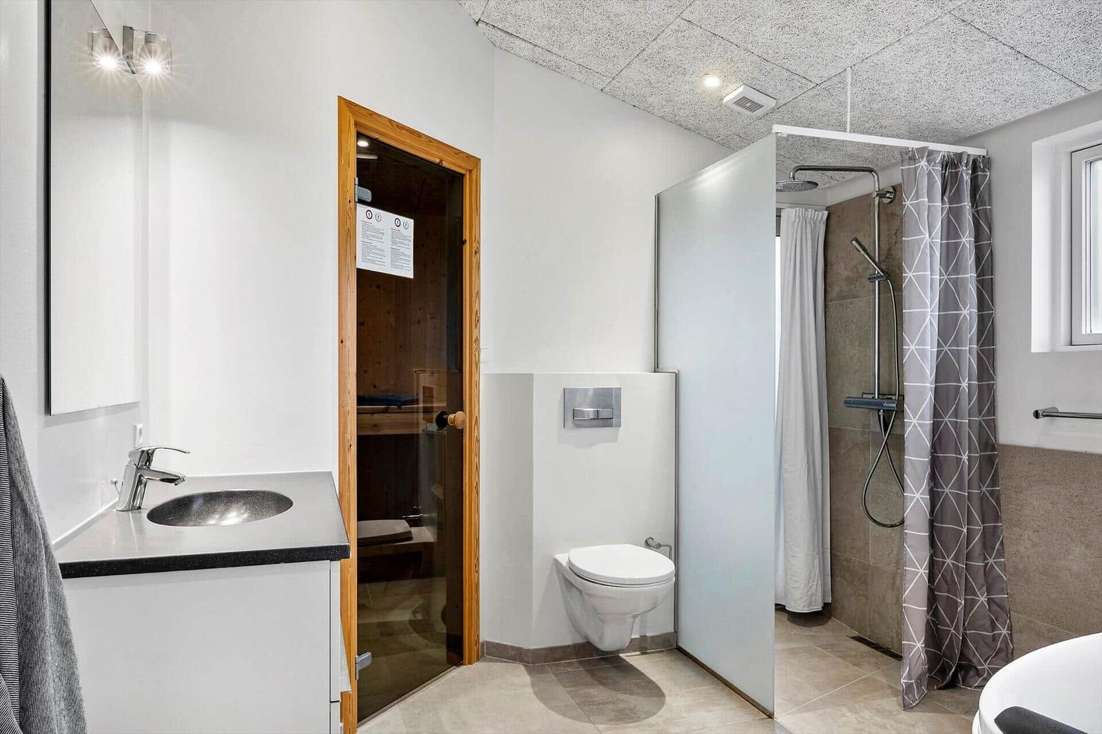 Bathroom with shower, toilet, and sink. Sauna is visible in the background.