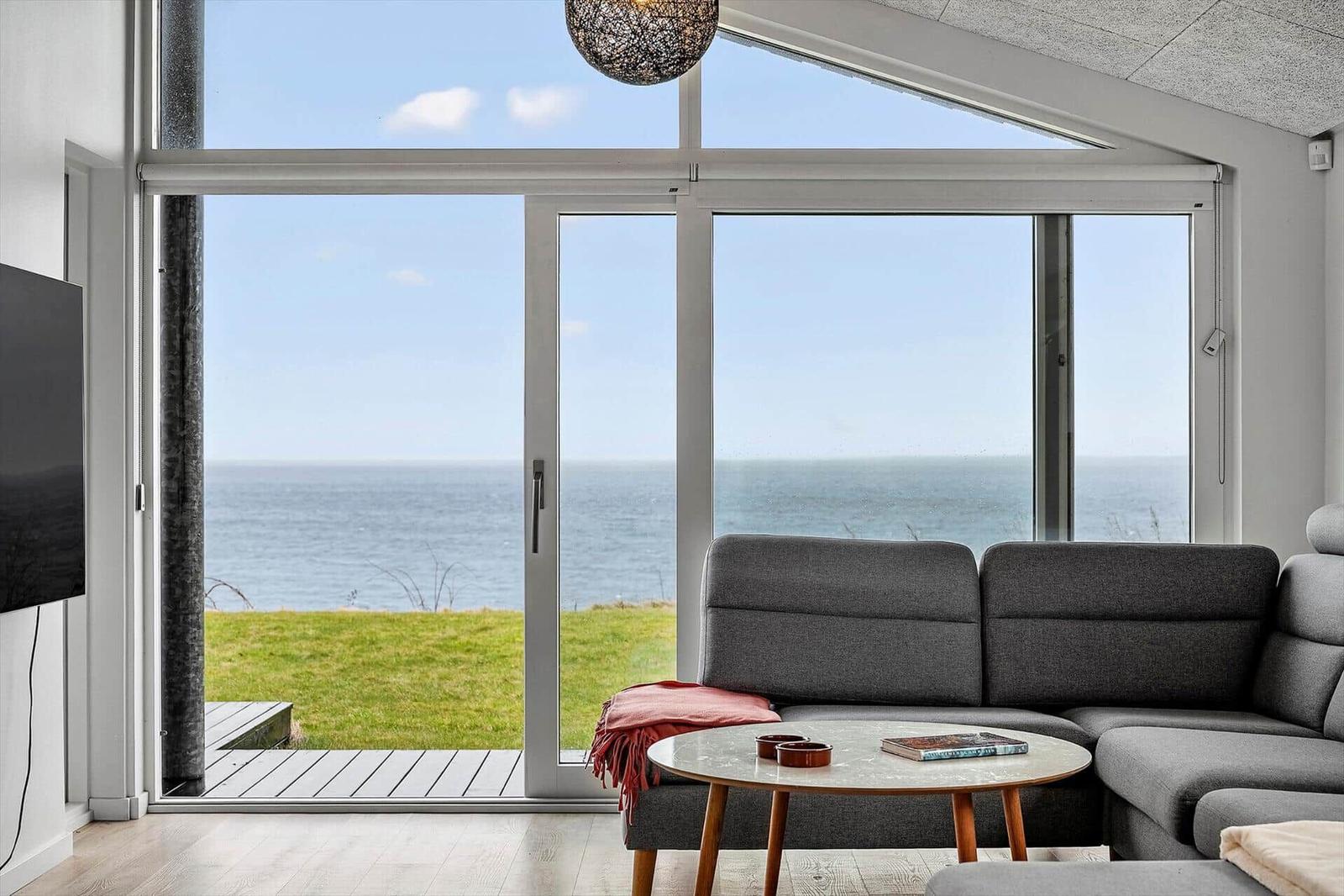 Living room with sea and grass view. Sofa, table, and windows visible.