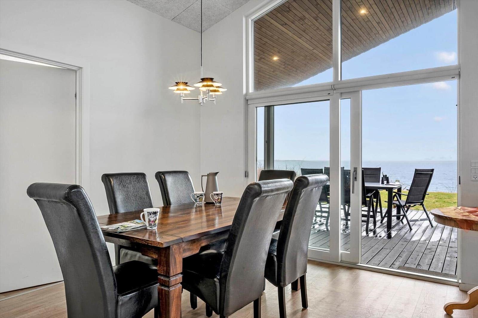 Dining room with table and chairs. Large glass doors lead to terrace with sea view.
