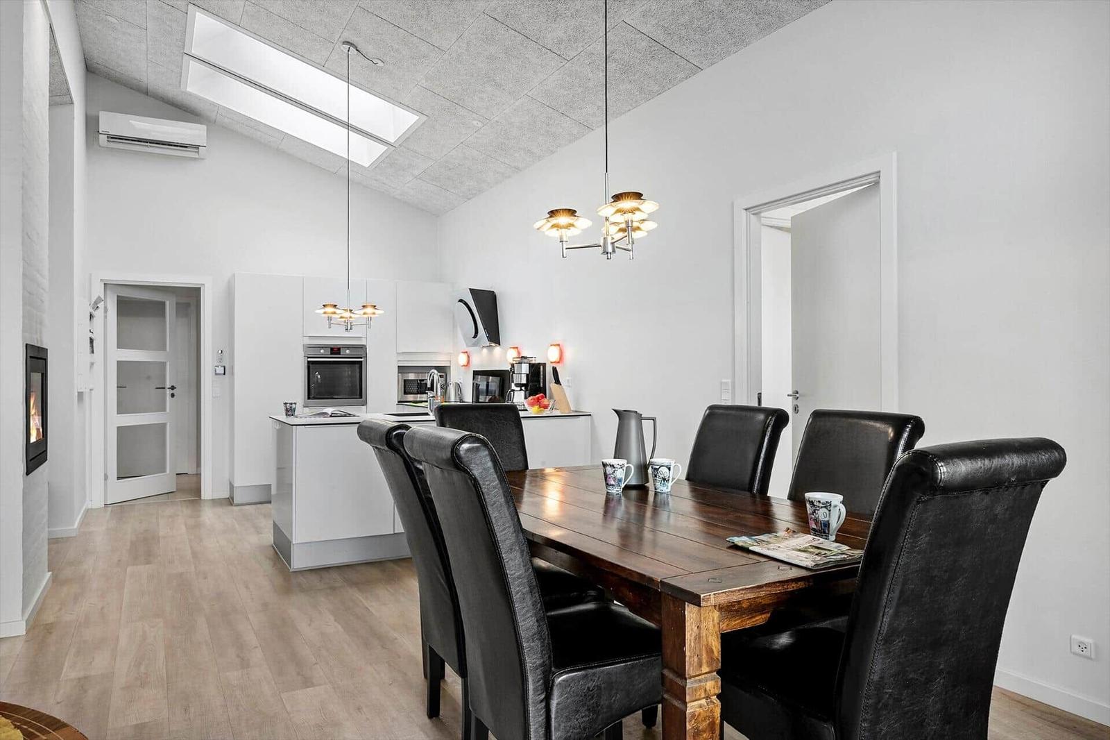 Dining area with wooden table and black leather chairs. Kitchen with white cabinets and range hood.