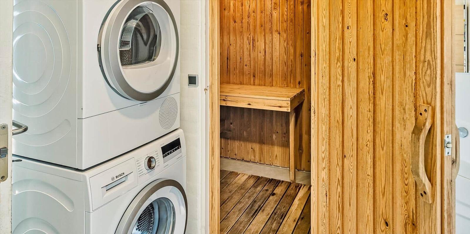 Dryer and washing machine next to a wooden sauna with bench.