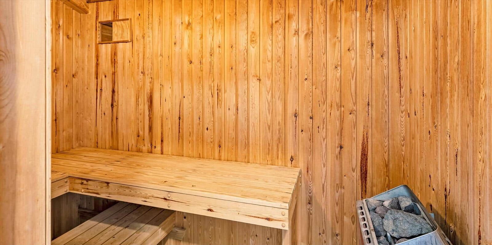 Sauna with wooden walls and bench, crate with stones on the right.