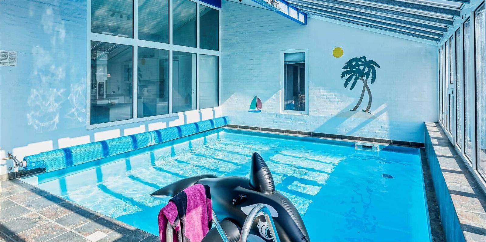 Pool with dolphin float and wall mural of palm trees and sun.