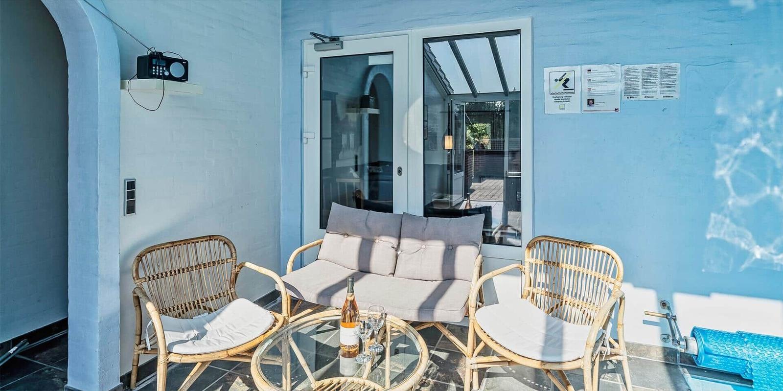 Terrace with rattan furniture, glass table, and bottle. Background: blue wall and glass door.