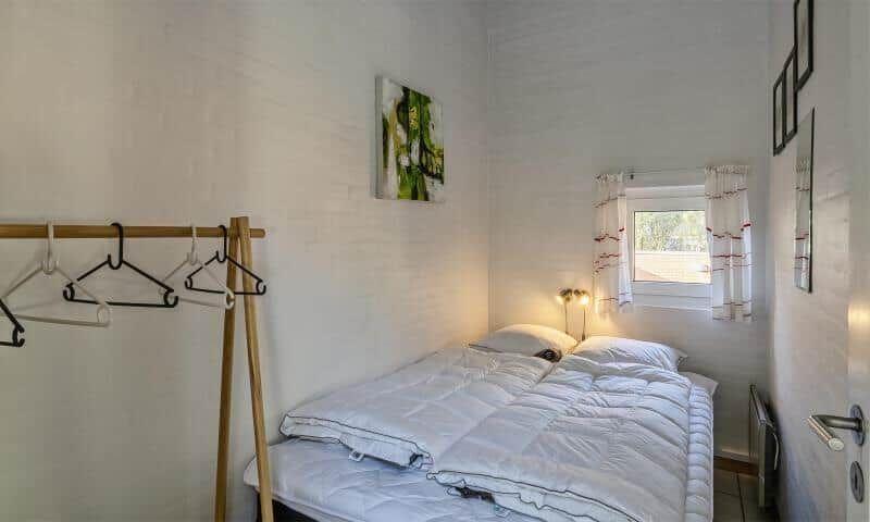 Bedroom with double bed, coat rack, and window with curtains.